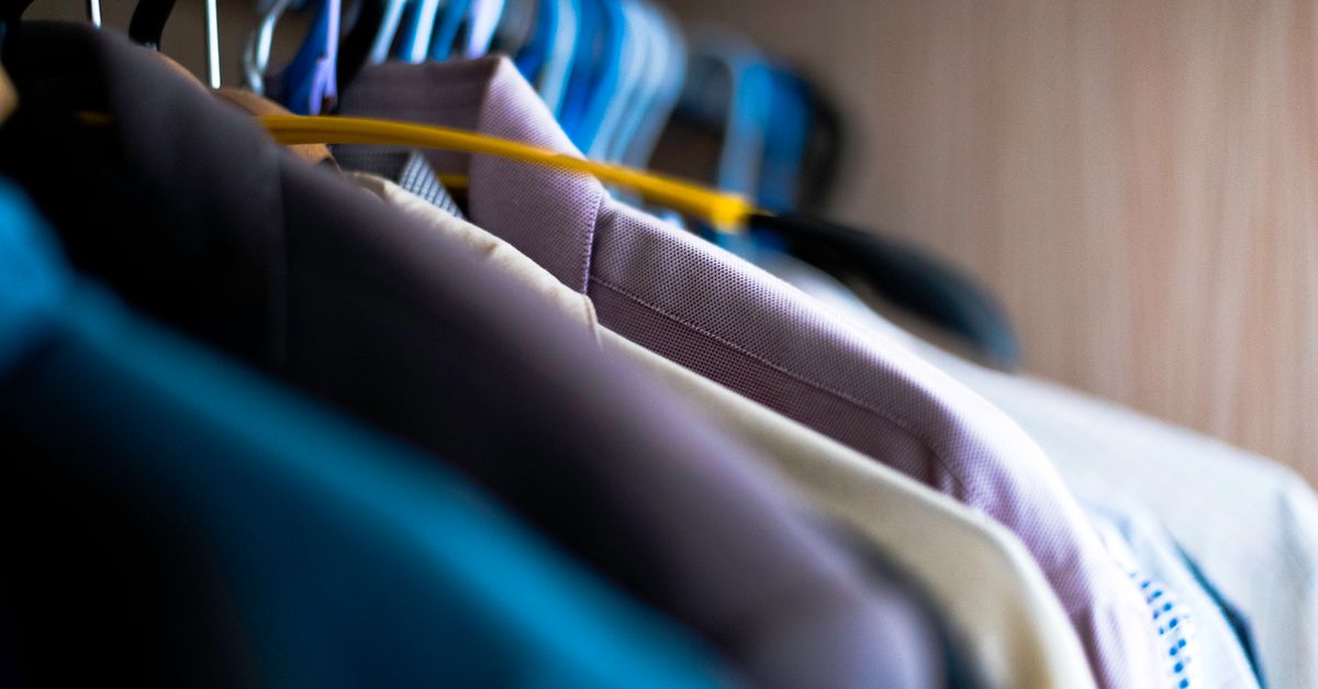 Close-up of various shirts hanging on colorful hangers inside a wardrobe.