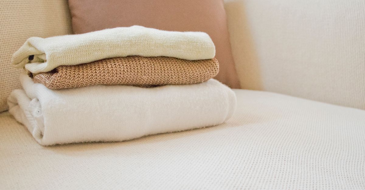 Soft folded sweaters in warm tones on a cozy cream sofa, showcasing home comfort and style.
