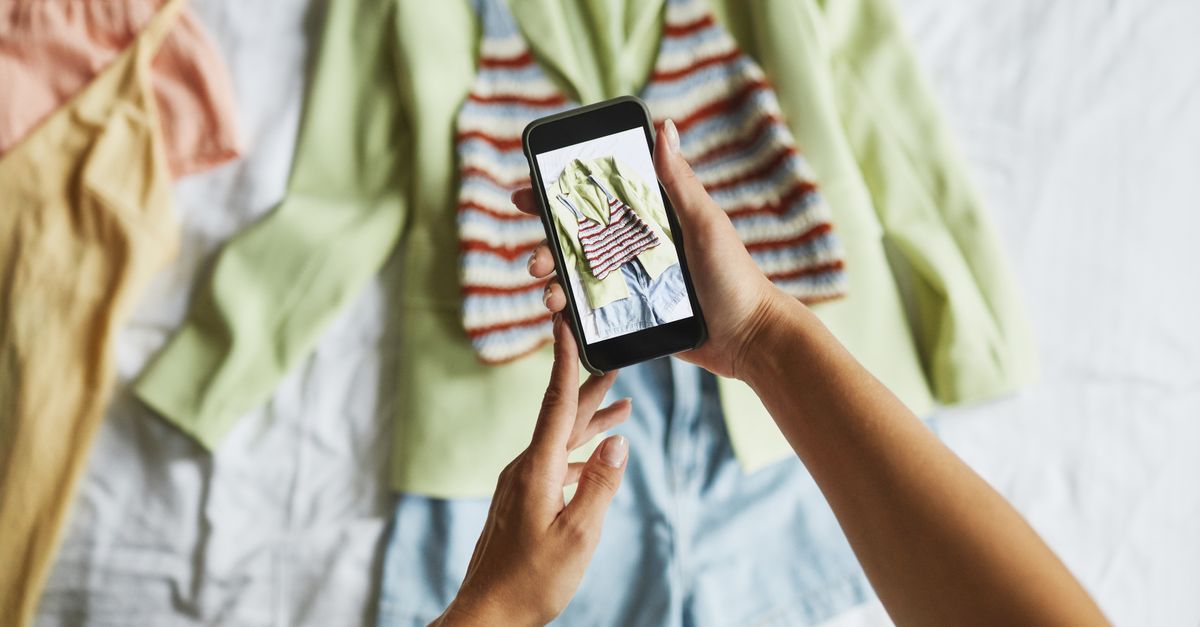 Hands taking photos of trendy outfit using smartphone on bed.