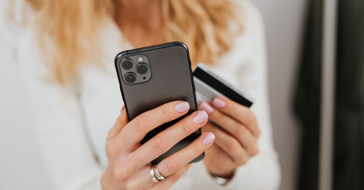 Close-up of woman holding smartphone and credit card for online transaction indoors.