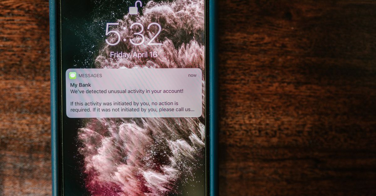 Close-up of a smartphone displaying a bank alert notification on a wooden table.