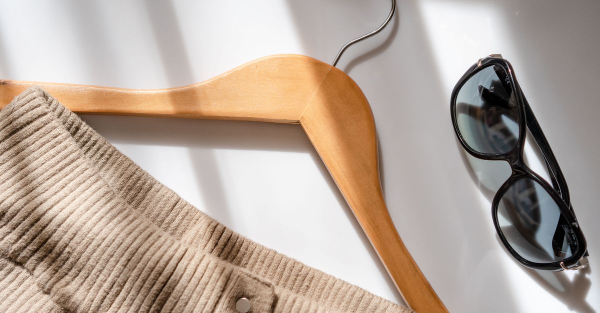 Flat lay of a corduroy skirt, sunglasses, and a wooden hanger on a white surface.