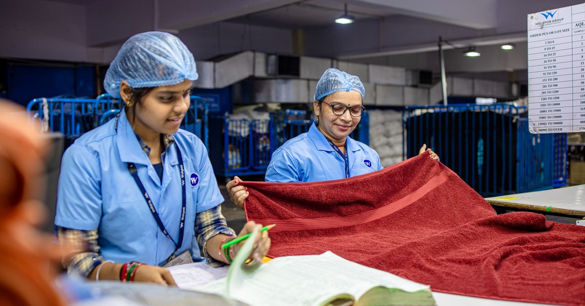 Two female textile workers inspecting red fabric in a factory setting.