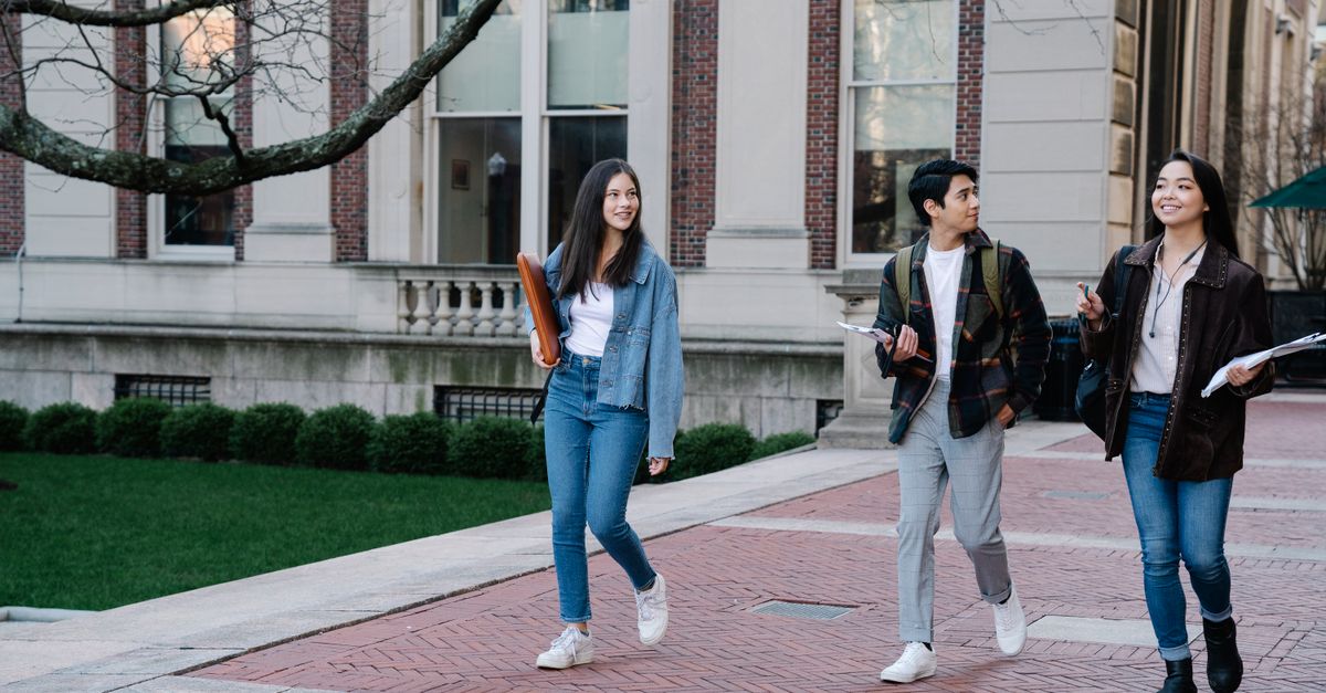 Group of young students walking on campus sidewalk on a bright day, showcasing casual university life.
