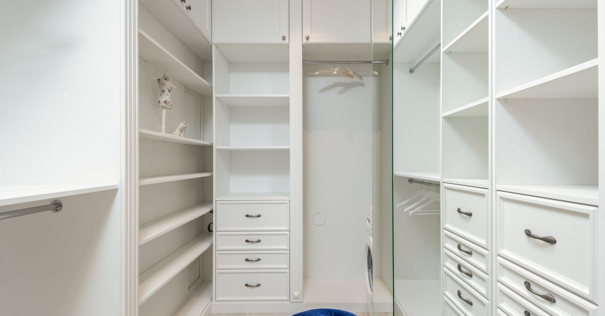 Soft blue velour pouf in white built in closet with empty shelves and racks in classic styled apartment