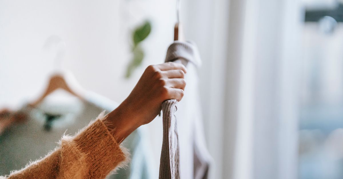 Crop unrecognizable female in sweater holding hanger with shirt while choosing clothes for work