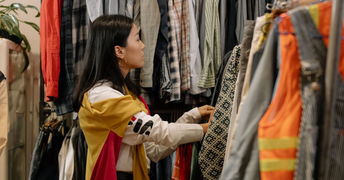 A young woman browsing clothes in a vintage store with colorful outfits.