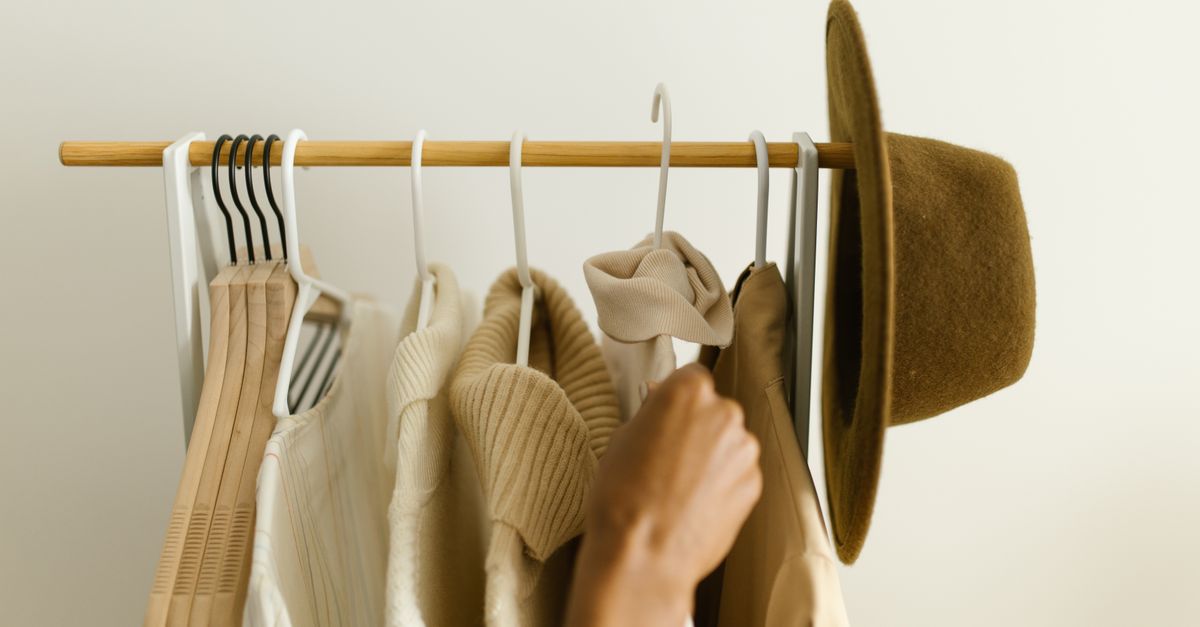 Stylish beige and brown clothes on a rack with a hand reaching in.