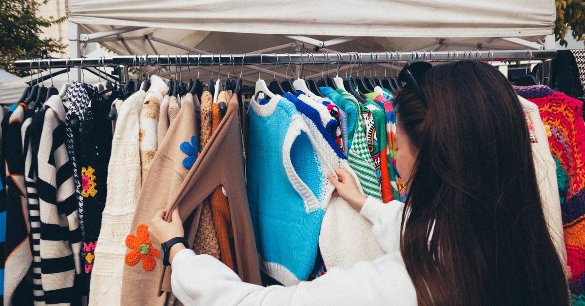 A woman browsing colorful vintage sweaters at an outdoor market stall.