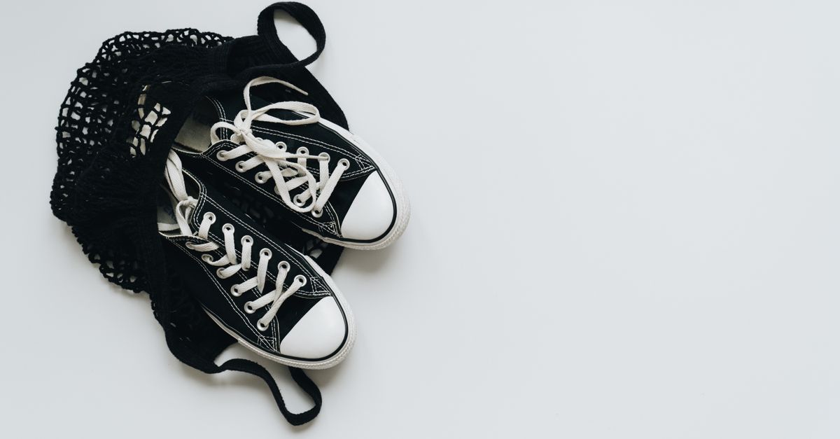 A pair of classic black sneakers in a black net bag on a white background, showcasing minimalism.